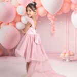 A young kid model in a pink high-low dress and tiara.