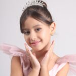 A young kid model in a pink dress and tiara, smiling.
