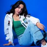 Young female model sitting casually on the floor, styled in denim and a sporty jacket.