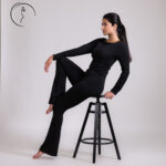 Woman in a black outfit leaning on a stool.