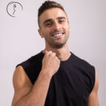 Male model in Kuwait smiling, wearing a black sleeveless shirt, hand near his chin.