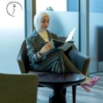 A hijabi model in suit reading a magazine.