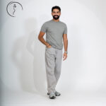 Full-length shot of a smiling man in a grey t-shirt, light grey jeans, and sneakers, with one hand in his pocket.