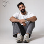 Man sitting on the floor in a white t-shirt and grey jeans.