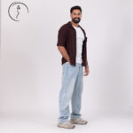 Smiling man in a brown shirt and light blue jeans.