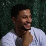 Kuwaiti male model smiling in a white t-shirt against a dark green textured background