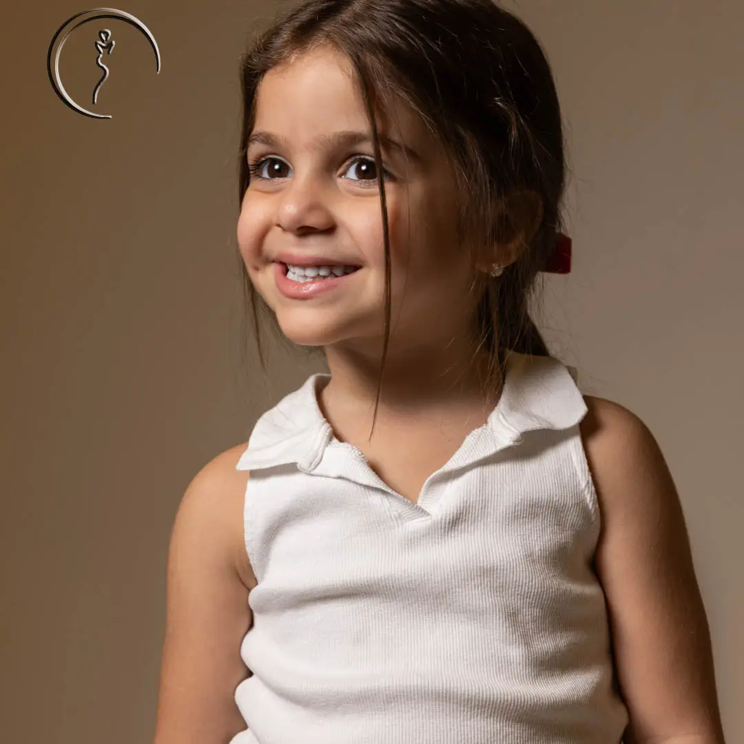Close-up of a young Kuwaiti female model in a white top, smiling with expressive eyes during a fashion portrait.