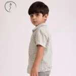 A young boy in a light green checkered shirt looks over his shoulder with a serious expression.