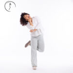 Woman in a white shirt and checkered pants playfully posing on one leg.