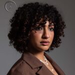 Woman in a brown jacket with a serious look.