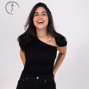 A candid, joyful shot of a woman with a big smile, wearing a black one-shoulder top with a gold chain accent.