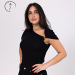 A woman posing in a black one-shoulder top with a unique asymmetrical neckline and a gold chain detail.