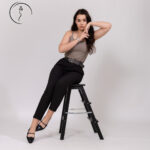 Elegant woman in taupe top and black trousers seated with hand pose