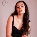 Stylish woman in black top with necklace posing under warm lighting