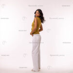 Female model in profile, green top, white wide-leg pants.