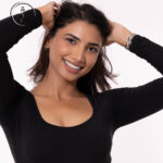 A close-up of a smiling female model with her hands in her hair.