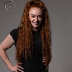 A smiling red-haired woman with her hands on her hips.
