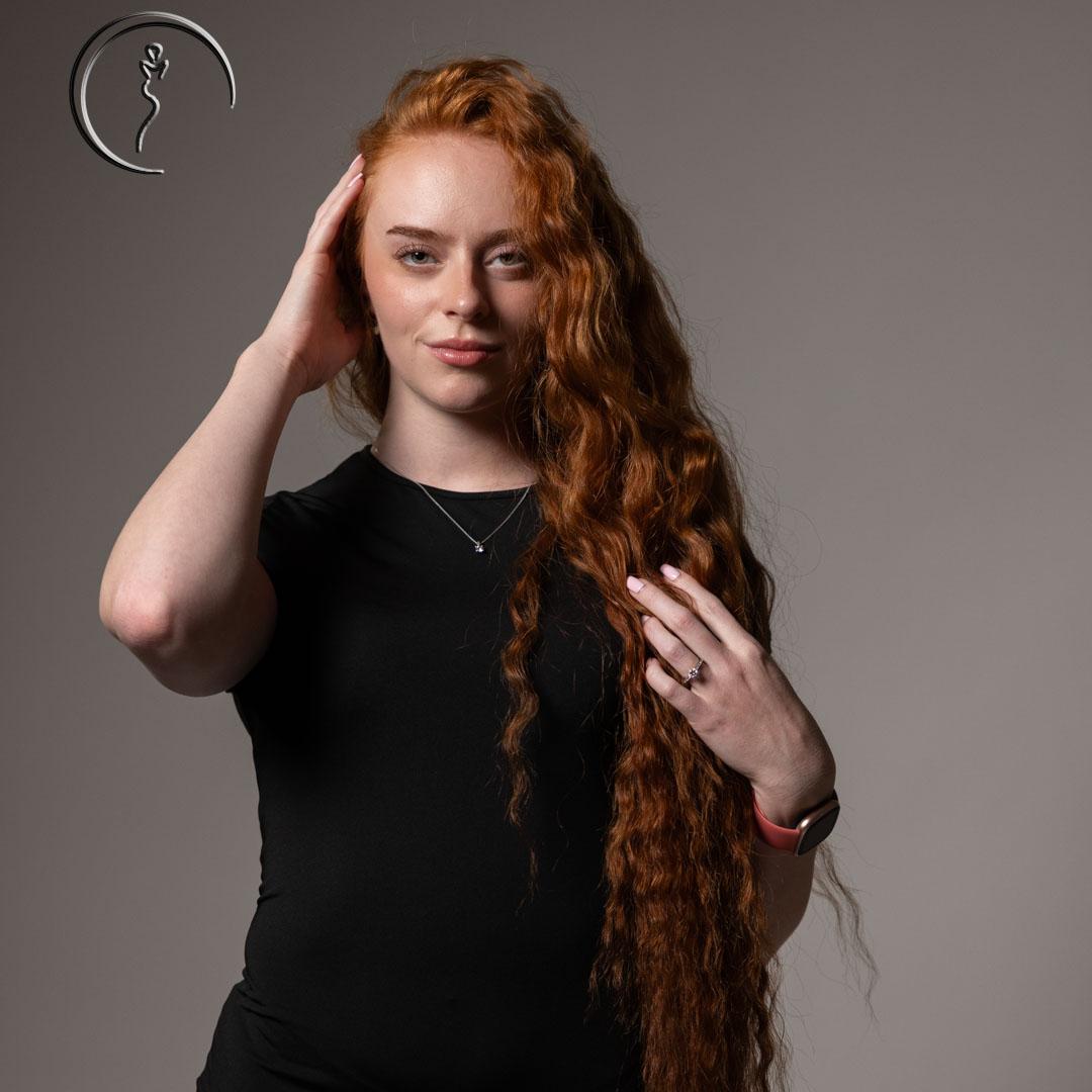 A red-haired woman touching her hair while looking at the camera.