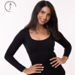 A female model in a black shirt smiling, with her hands on her hips.