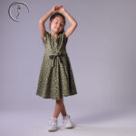 Kid fashion model in a green floral dress, posing with arms raised gracefully.