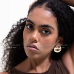 Curly haired female model in Kuwait with hands in her voluminous hair, brown top – Model 689