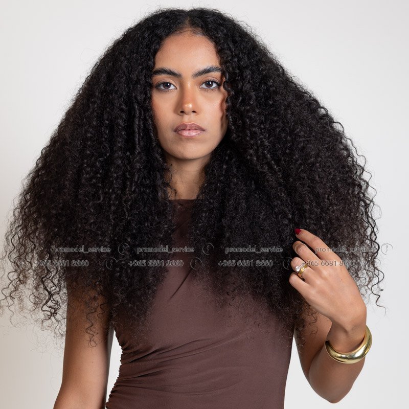 New curly haired model in Kuwait in black top, playful hand-in-hair portrait – Model 689