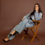 Full-length fashion shot of a female model in Kuwait in double denim and heels, seated on a wooden director chair – Model 690