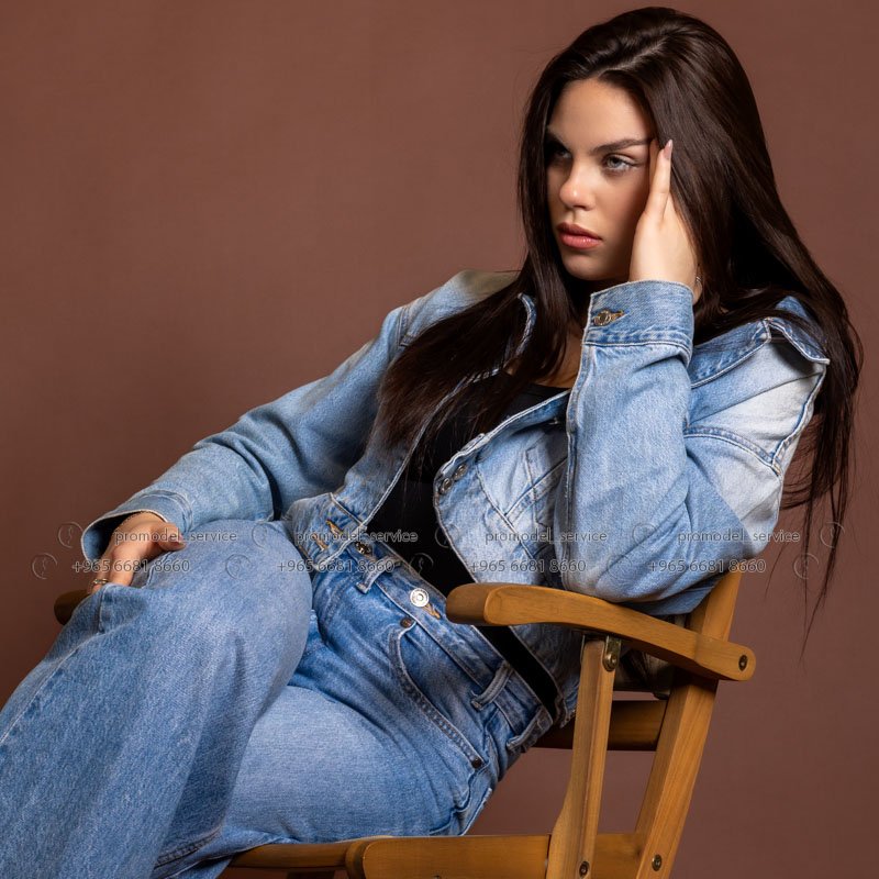 Fashion model in Kuwait seated in a director chair in a denim jacket, hand in her hair – Model 690